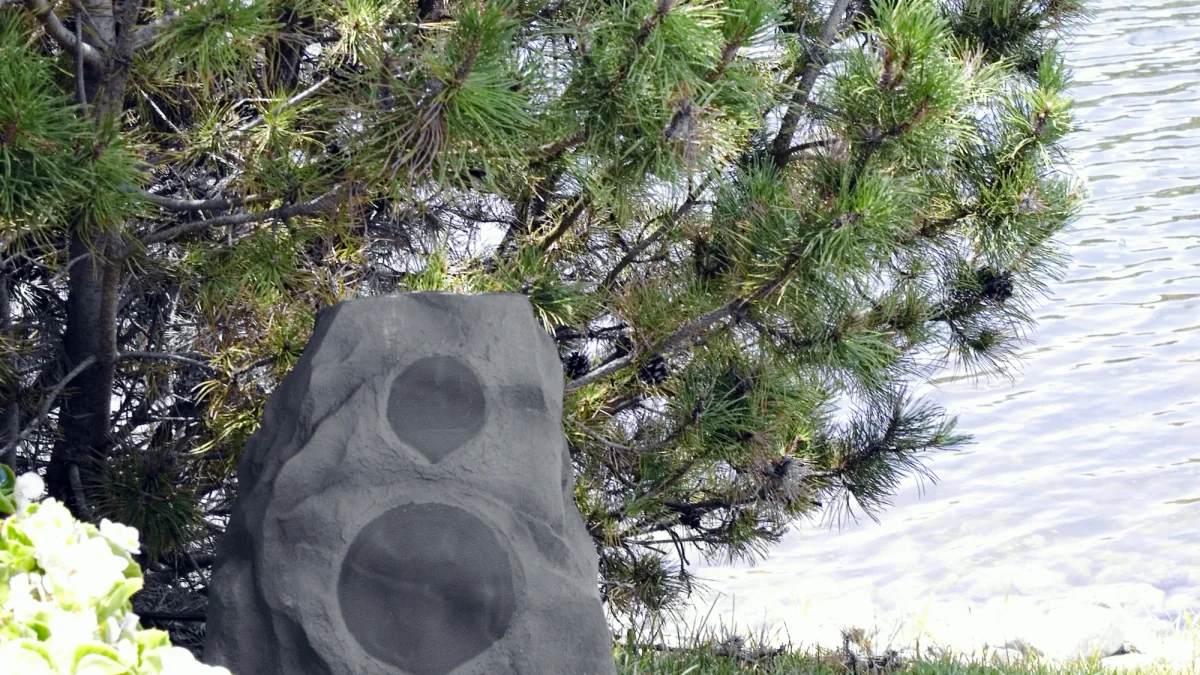 Caixa de som com acabamento de pedra instalada junto ao paisagismo