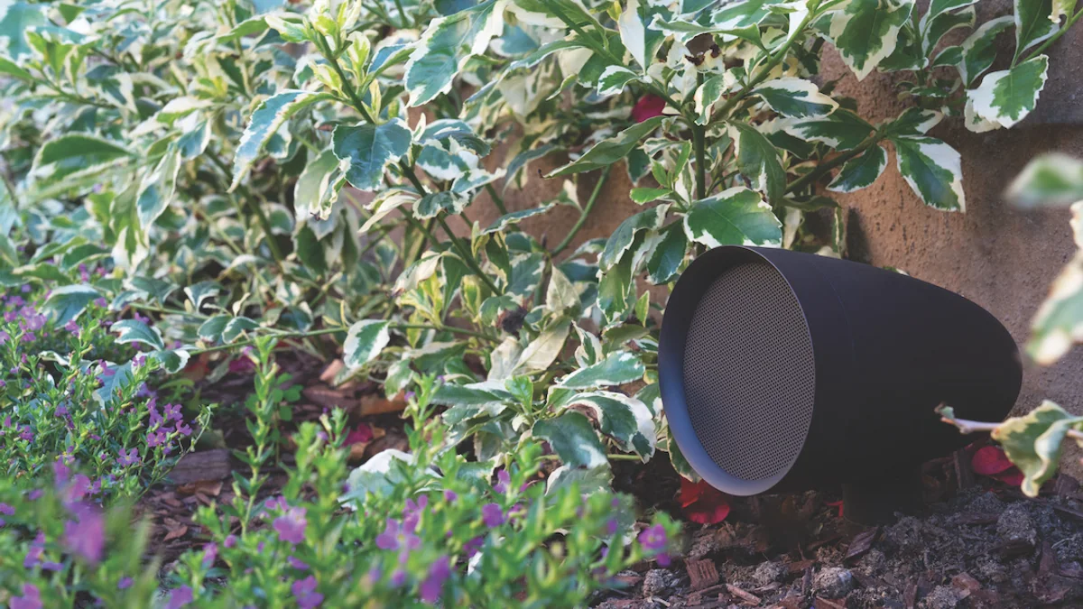 Caixa de som externa do tipo satélite instalada entre plantas no jardim